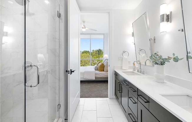 A bathroom with a walk-in shower, a vanity with a mirror, and a view of a backyard through the door.