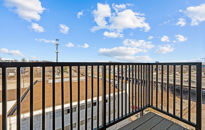 A balcony with a black railing and a view of a train track and a building.