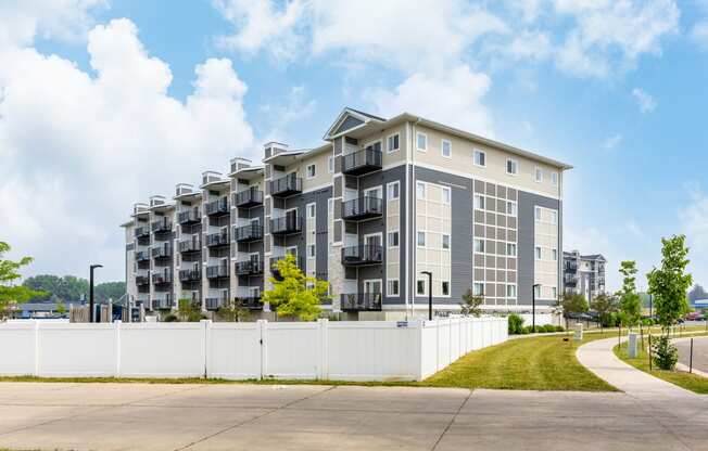 a grey apartment building with balconies and a white fence in front of it