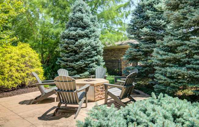 A patio with chairs and a table surrounded by greenery.