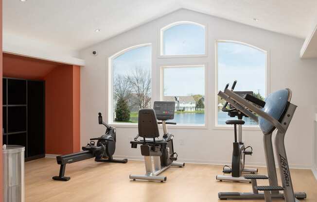three exercise machines in a room with three large windows