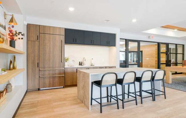 A kitchen in the clubroom with a faux wood fridge, white quartz countertops, and a large island with rattan-back bar stools.