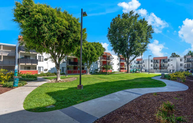 a park with grass and trees in front of apartment buildings