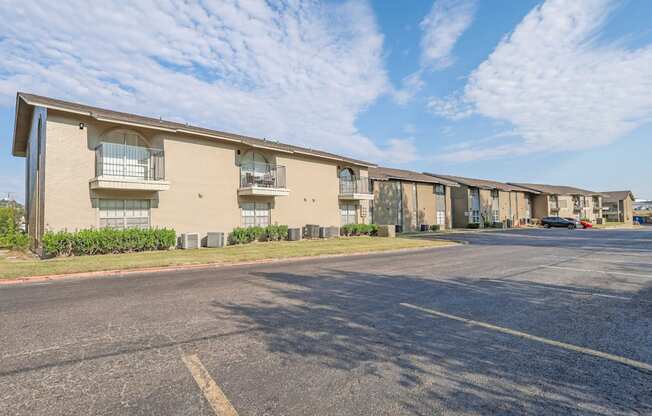 A parking lot in front of an apartment building with a blue sky and clouds in the background at The Creole Apartments in Shreveport, LA