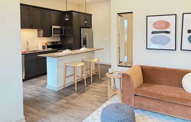 a furnished modern living room next to a spacios kitchen with dark cabinets in the guest suite