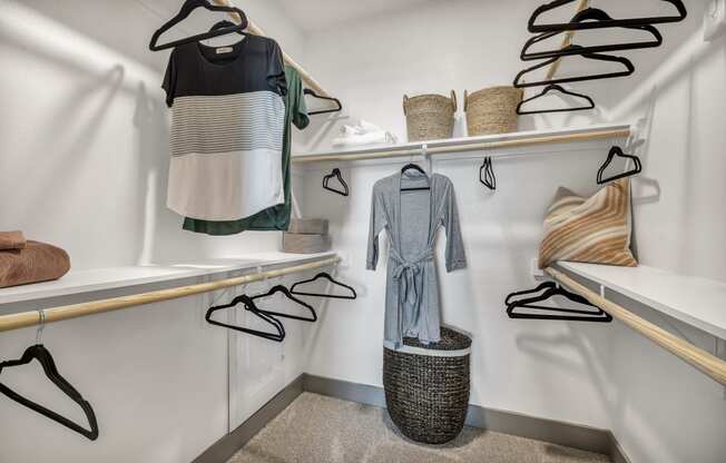 a walk in closet with white walls and shelves and clothes hanging on a rack
