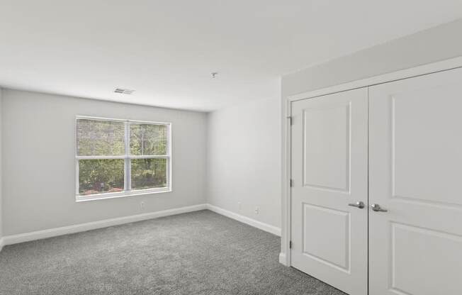 A room with a carpeted floor, a window, and a white door.