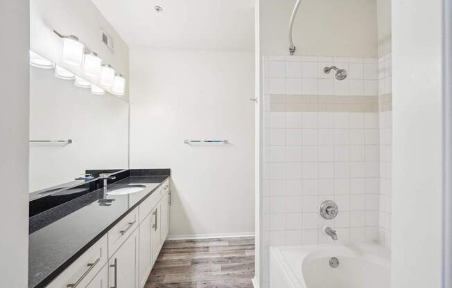 A white bathroom with a black counter top and a white bathtub.