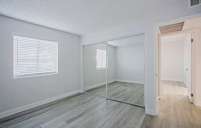 an empty bedroom with a mirrored closet and a large window