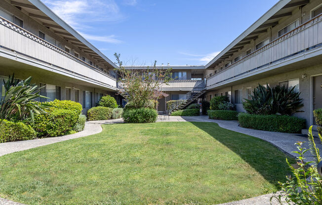 the courtyard of an apartment building with a green lawn and bushes