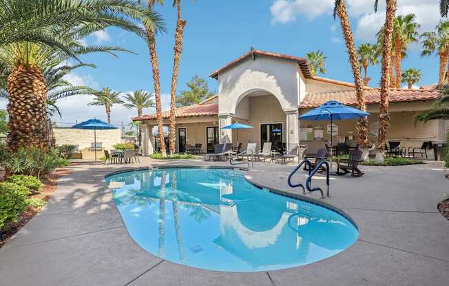 A pool surrounded by palm trees and a building in the background.