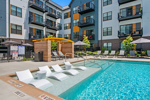 a swimming pool with lounge chairs in front of an apartment building