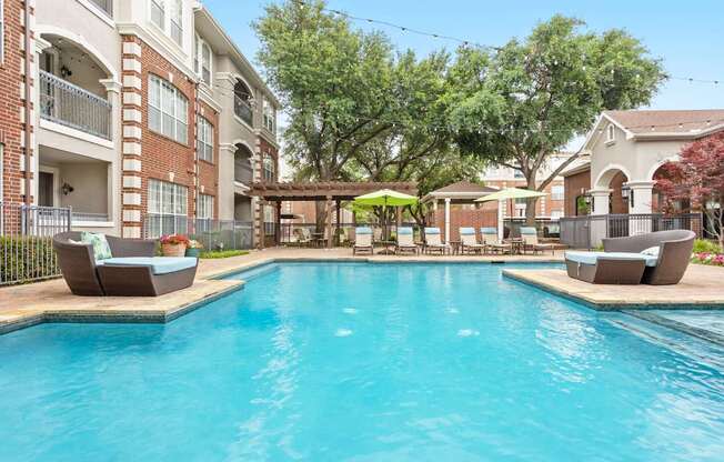 A large swimming pool surrounded by lounge chairs and umbrellas in a residential area.