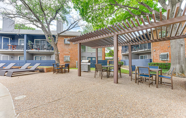 A patio with a pergola and chairs is surrounded by apartment buildings.