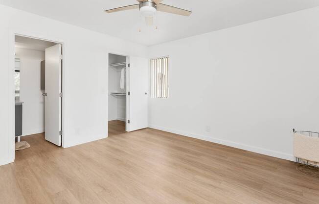 A room with a ceiling fan and light fixture, two open doors, and a chair.