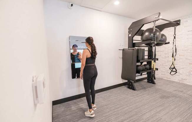 A woman is standing in a gym looking at a mirror.