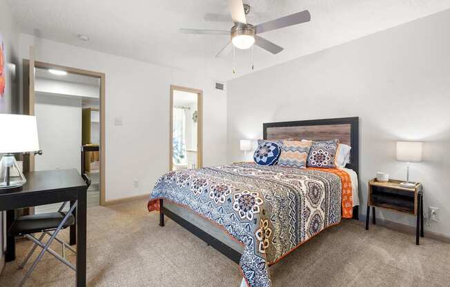 A bedroom with a bed, desk, chair, and ceiling fan.