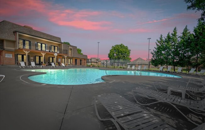 A large outdoor swimming pool surrounded by lounge chairs and a building with a balcony.