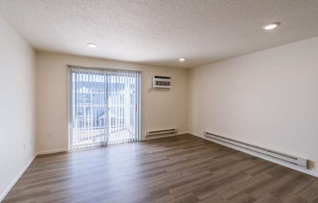 the living room of an empty apartment with wood flooring and a balcony. Fargo, ND Stonebridge Apartments