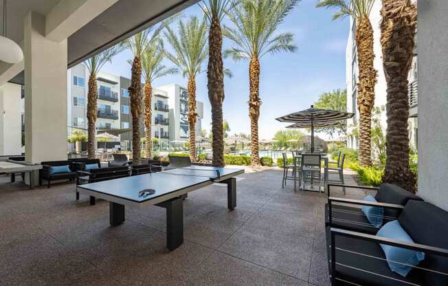 a patio with a ping pong table and chairs with palm trees in the background