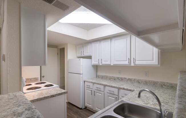 A kitchen with white cabinets and appliances in a 717 square foot 1 bedroom, 1 bath loft apartment home at Canyon Creek Apartments in Dallas Midtown neighborhood of Dallas, TX.