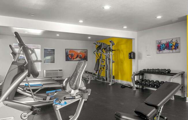 A gym with a rowing machine, a bench press, and a yellow wall.