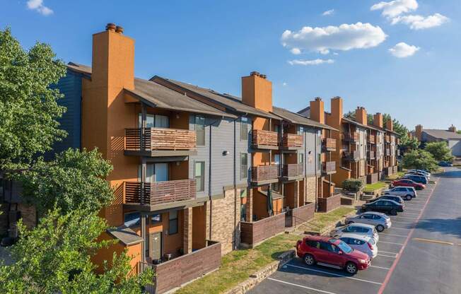 A row of apartment buildings with cars parked in front.