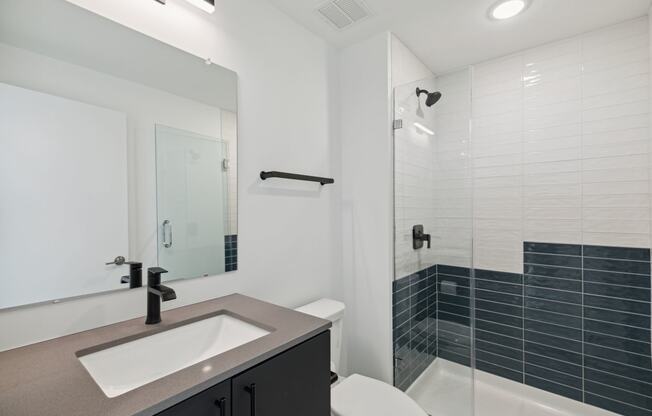 Sleek bathroom design featuring a vanity with a large mirror, white and navy blue tiles, and a shower-tub combo accented with modern fixtures.