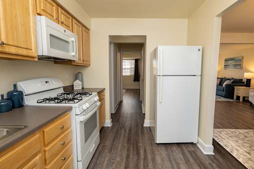 A white refrigerator stands in a kitchen with wooden cabinets and a stove.