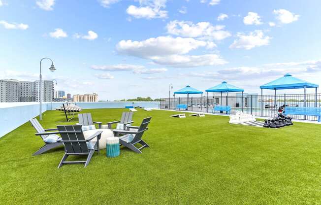 A lawn with chairs and umbrellas is in the foreground with a pool and apartment buildings in the background.
