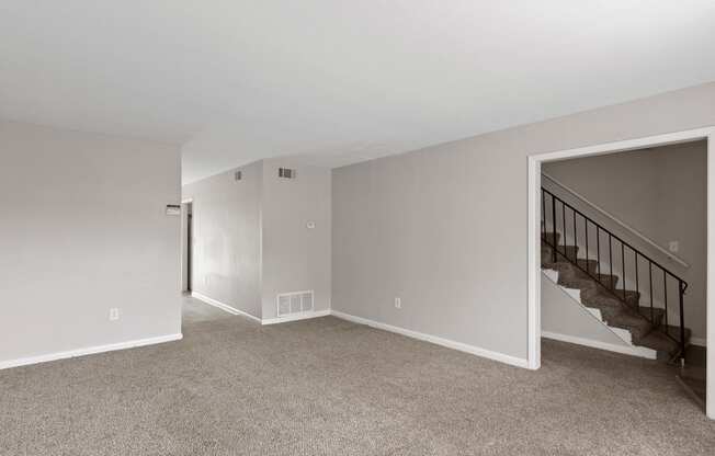 an empty living room with carpet and stairs in a house