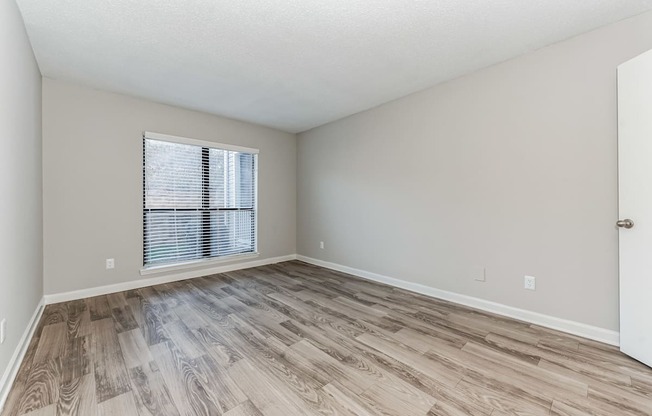 A room with wooden flooring and a window with blinds.