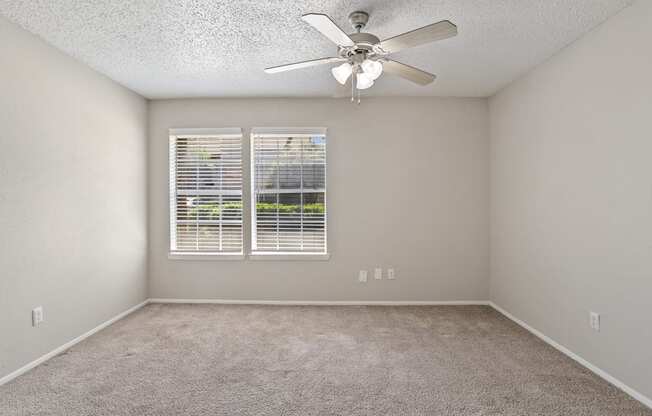 a bedroom with a ceiling fan and two windows