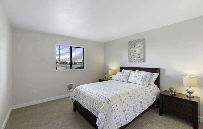 Bedroom with a Large Bed and Two Nightstands, Tan Carpeting, and Window at Campo Basso Apartment Homes, Lynnwood