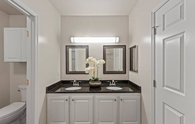 a bathroom with white cabinets and a black counter top with two sinks