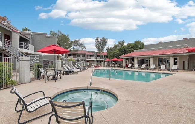 A pool area with a red umbrella and lounge chairs.