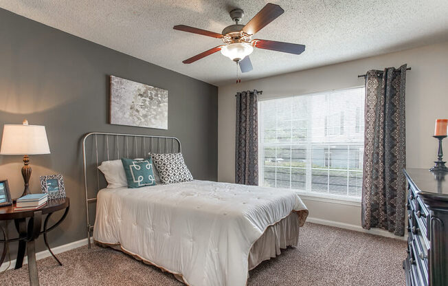 A bedroom with a bed, a ceiling fan, and a window with curtains.