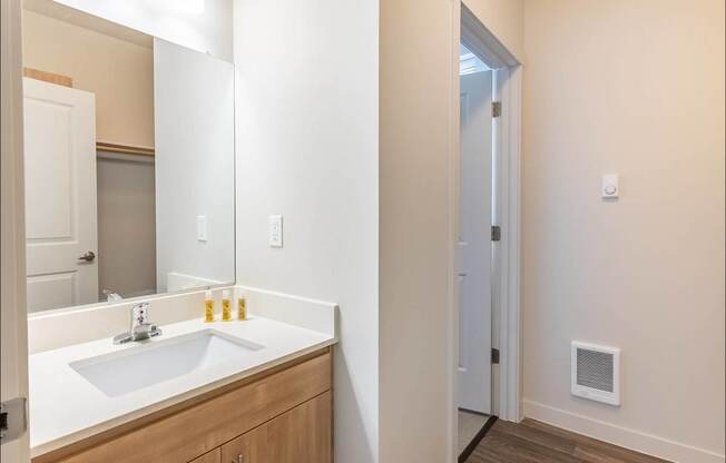 A bathroom with a sink, mirror, and a door at Forestplace Apartment Homes, Forest Grove, Oregon