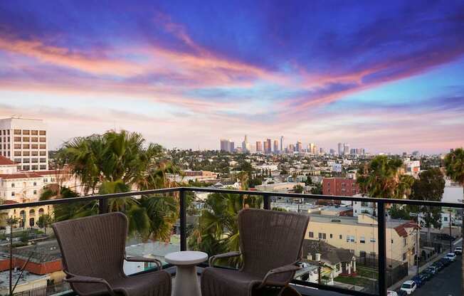 Two chairs and a table are set up on a balcony overlooking a city skyline.