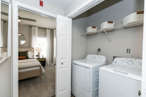 a white washer and dryer in a room with a bed and a mirror