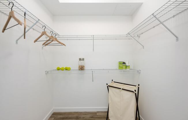 room with white walls and a white closet with hanging racks and a shelf with towels
