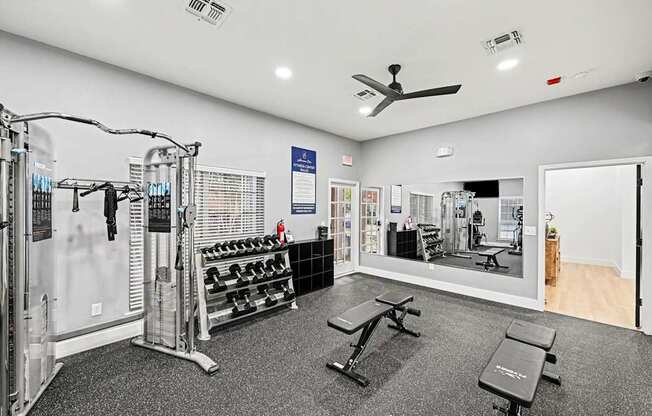 A gym with a variety of equipment including a weight bench, dumbbells, and a squat rack.