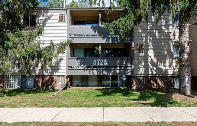 an apartment building with a sidewalk and trees in front of it