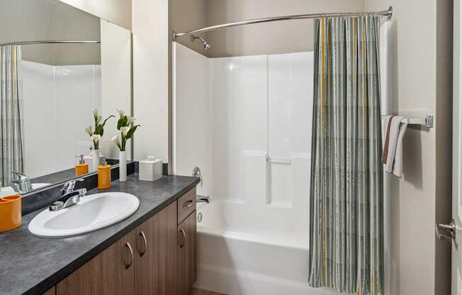 A bathroom with a sink, mirror, and shower.