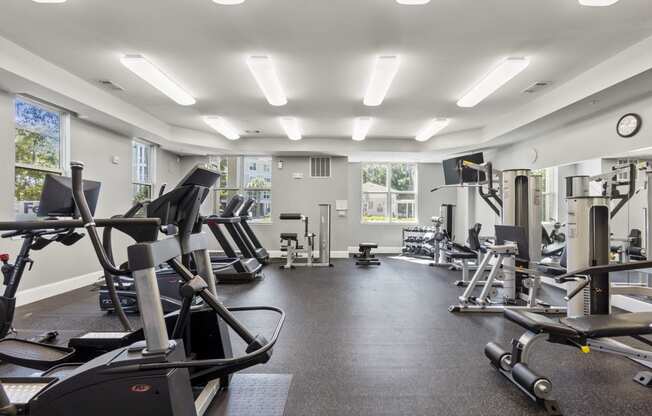 a gym with cardio equipment and weights on the floor and windows