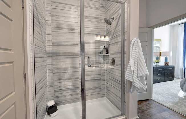 A modern bathroom with a glass shower enclosure and a white towel hanging on the door.