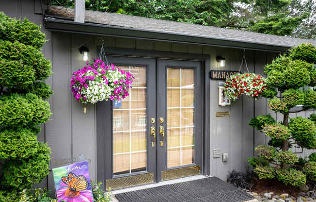 the front of the leasing office with two doors and flowers hanging on the side