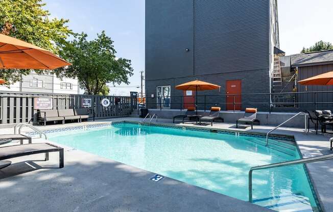 a pool with lounge chairs and umbrellas in front of a building