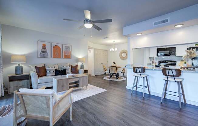 A modern living room with a white ceiling fan and a kitchen area in the background.