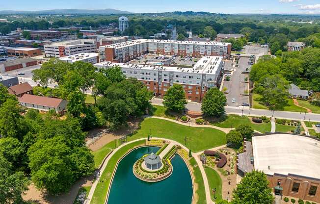 A large building complex with a fountain in the middle of a green area.